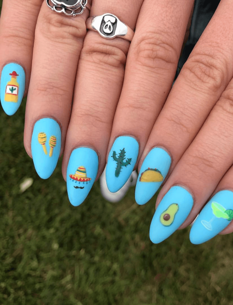 Pastel blue nails featuring Cinco de Mayo-themed icons such as a sombrero, cactus, taco, and avocado, paired with Mexican-inspired jewelry.
