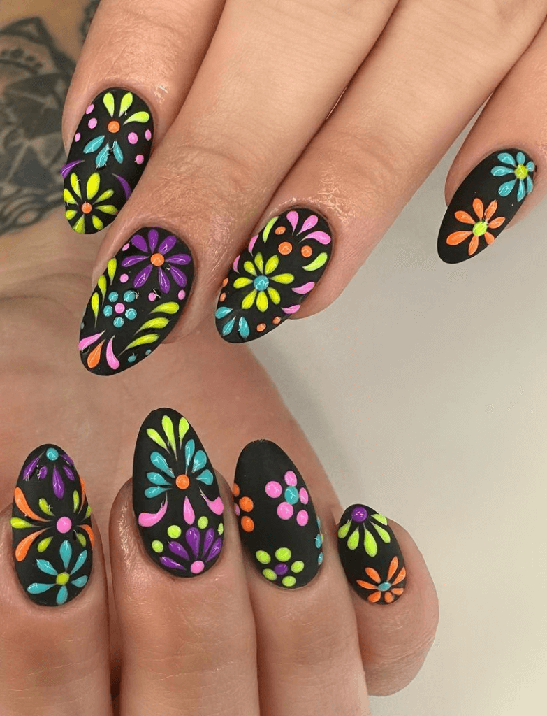Nails with a black base featuring a Cinco de Mayo nails design of colorful, neon floral patterns reminiscent of a night celebration.