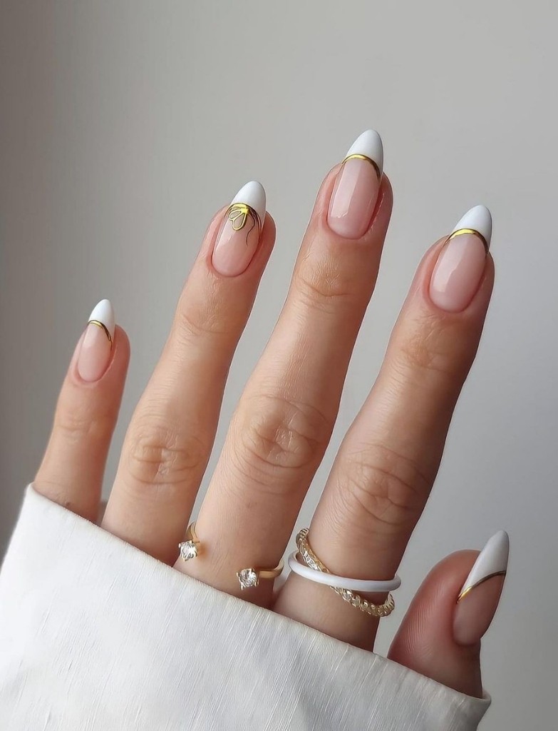 Wedding French nails with a modern twist, featuring a clear pink base and crisp white tips outlined by a sleek gold chrome strip, adorned with an array of delicate rings for a complete bridal hand look.