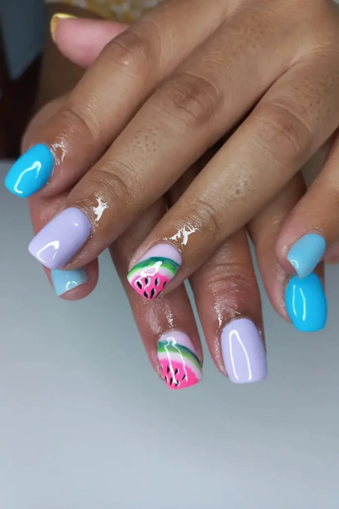 Hands with Watermelon Nail Designs featuring pastel blue and purple nails with an accent nail showing a watermelon slice pattern.